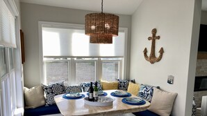 Un coin repas avec une table dressée pour quatre personnes, un luminaire suspendu en fibres tressées et un élément décoratif en forme d’ancre fixé au mur.