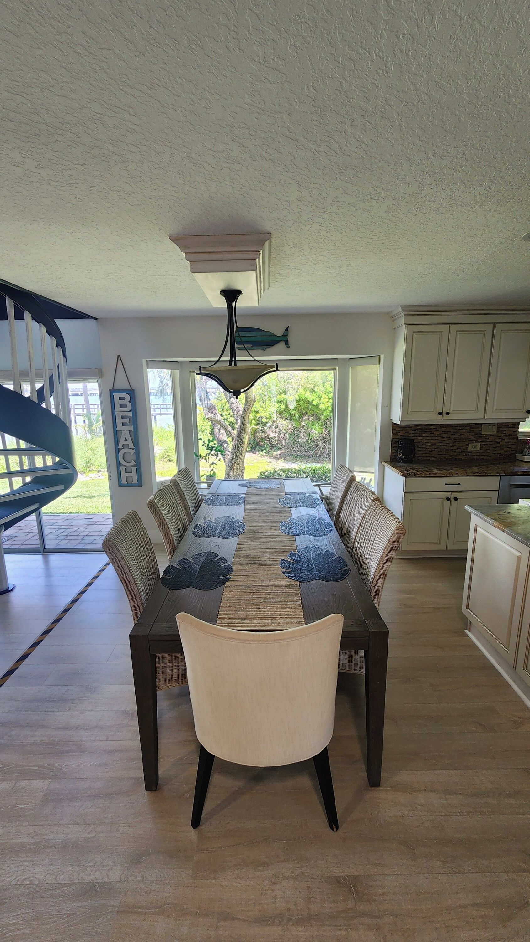 Comedor con una mesa larga, sillas, un ventilador de techo y vistas al exterior.