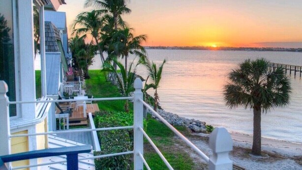 Una terrazza con ringhiera che si affaccia su uno specchio d'acqua al tramonto.