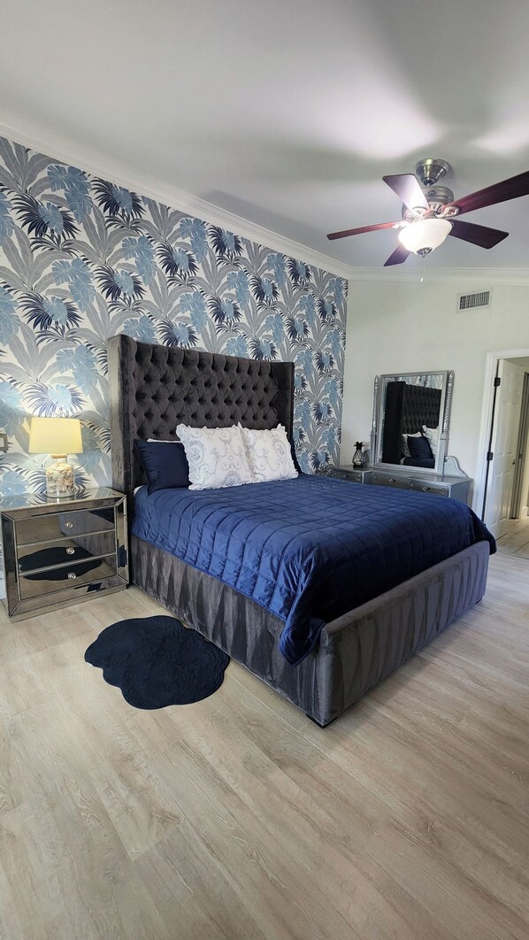 A bedroom with a large bed, a ceiling fan, and a patterned wallpaper.