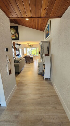 A hallway with wooden flooring, a staircase, a dining area with a table and chairs, and a white refrigerator. - Amazing 5 Bedroom, 3-bathroom Beach house. Bring the whole family and friends. (Jensen Beach)