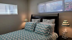 Un dormitorio con cama, dos lámparas de noche, una ventana con persianas y un ventilador de techo.