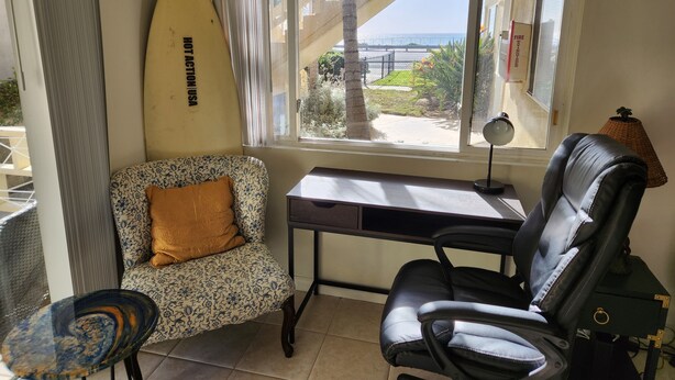 Una habitación con escritorio, dos sillas, una tabla de surf y vista al océano.