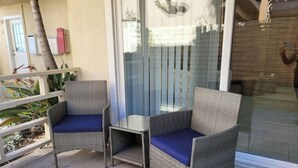 Dos sillas de mimbre con cojines azules en un balcón con puerta de cristal y vista a un edificio.