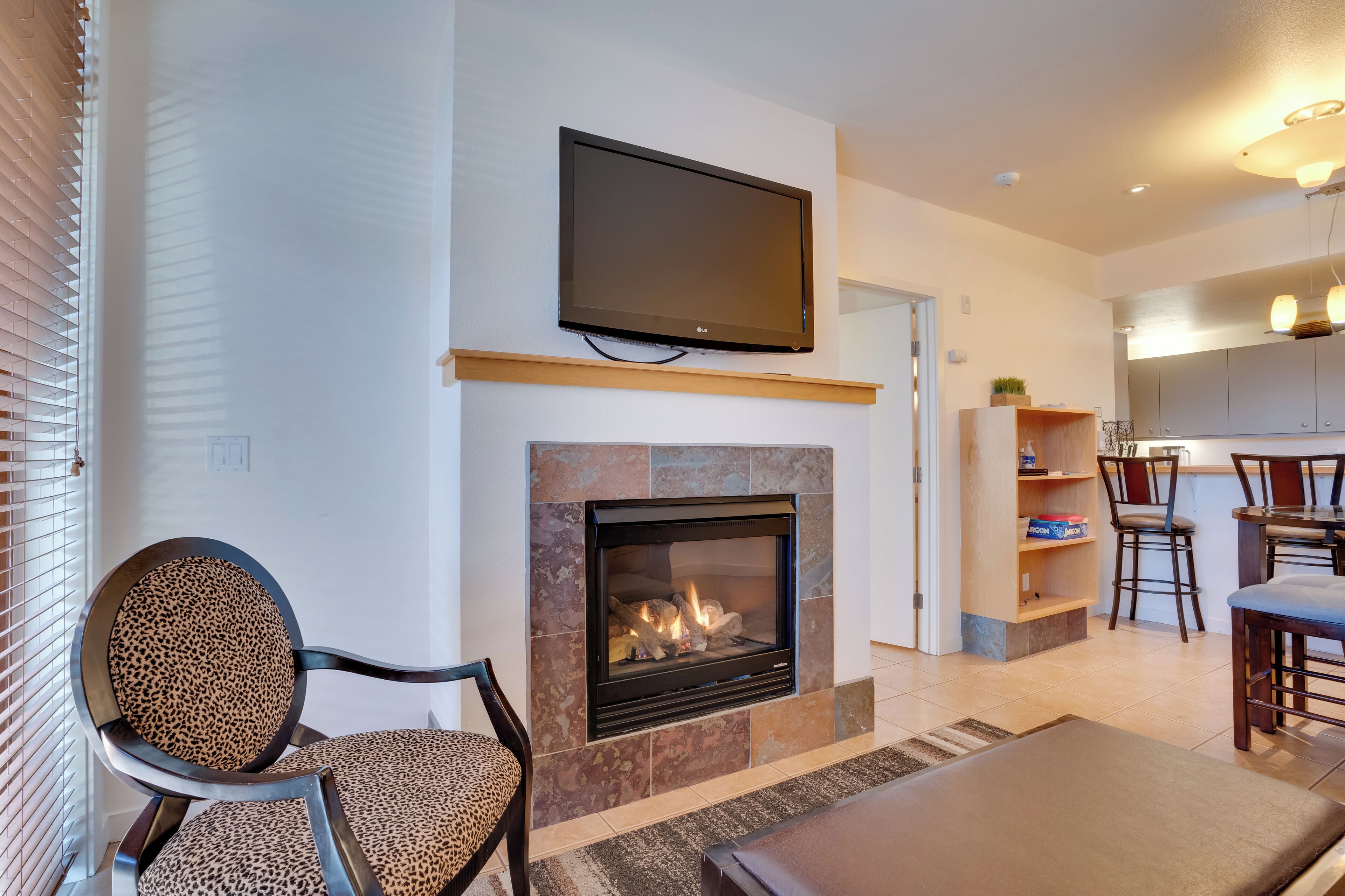A living room with a fireplace, a flat-screen TV mounted above it, and a dining area with chairs and a table.
