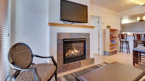 A living room with a fireplace, a flat-screen TV mounted above it, and a dining area with chairs and a table. - Resort-Style Condo w/ Lake Chelan & Mtn Views (Chelan)