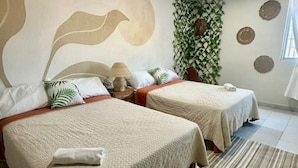 A room with two beds, each with a white bedspread and a pillow with a palm leaf pattern. There is a small table with a lamp between the beds, and a woven basket on the wall. - Residencial Edzna (Campeche)
