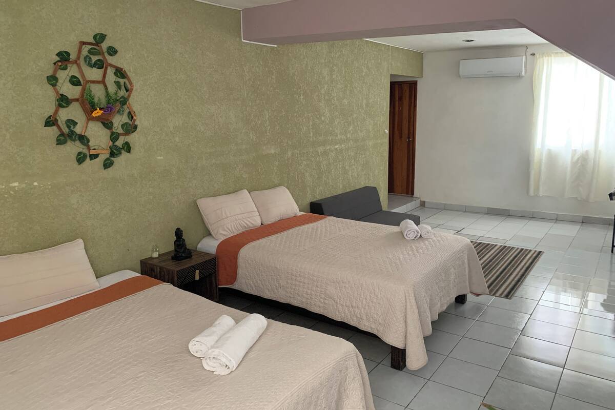 A hotel room with two beds, a green wall, a wooden decoration, and a view of the outside.