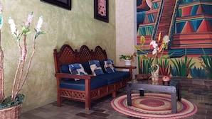 A room with a wooden sofa, a small table, and a colorful mural on the wall. - Residencial Edzna (Campeche)
