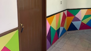 A hallway with a brown door, tiled floor, and a colorful geometric wall design. - Residencial Edzna (Campeche)