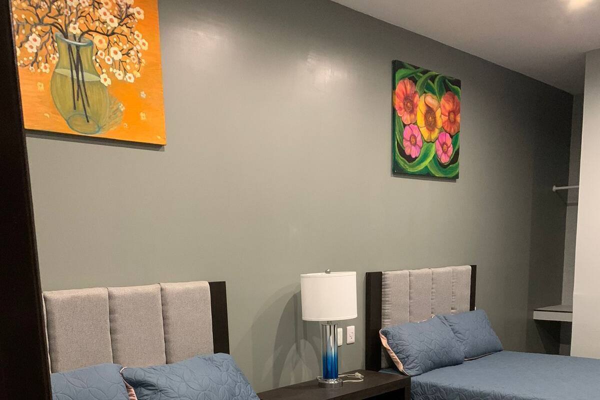 A hotel room with two beds, each with a headboard, a nightstand with a lamp, and artwork on the walls.