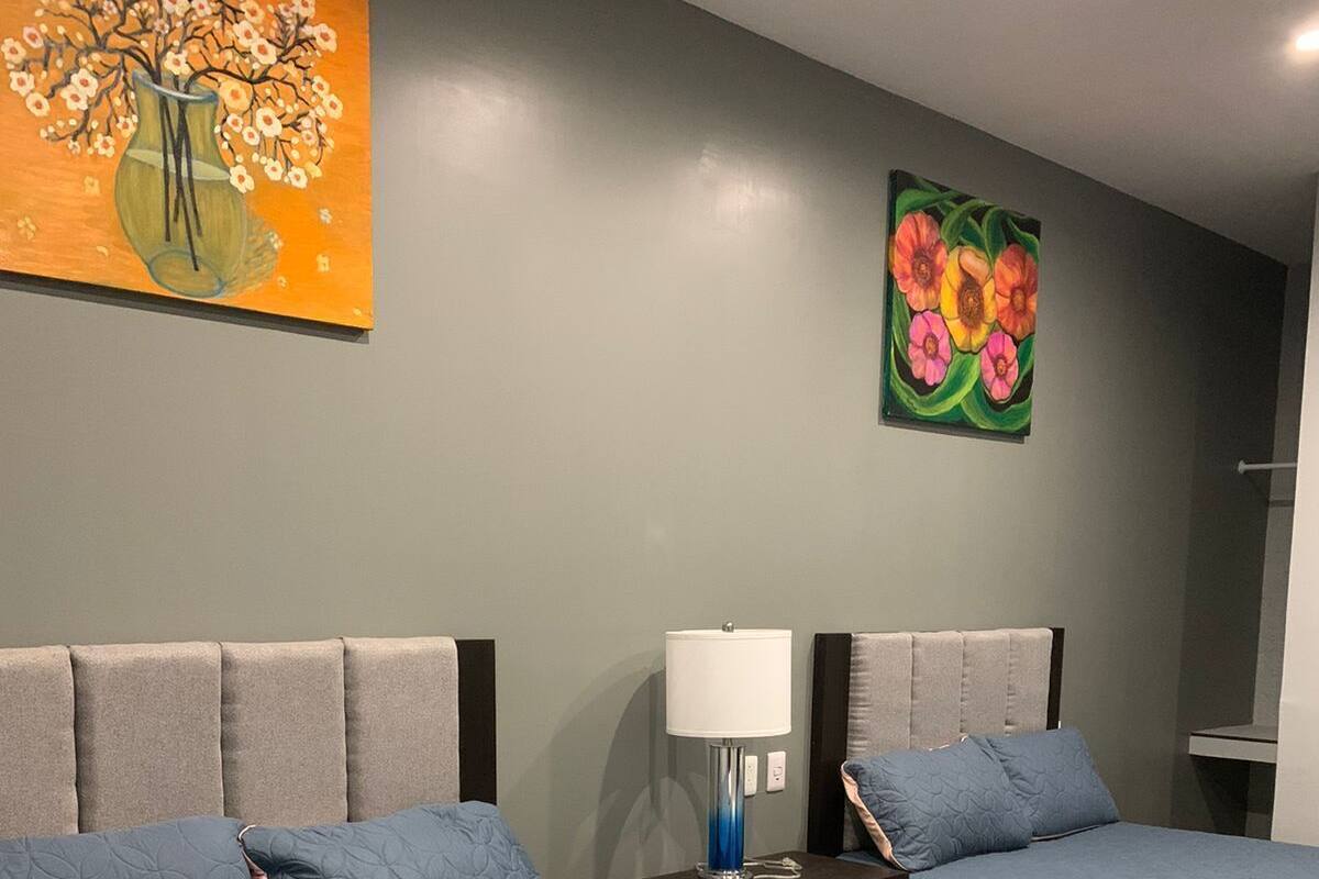 A hotel room with two beds, a nightstand, a lamp, and two paintings on the wall.