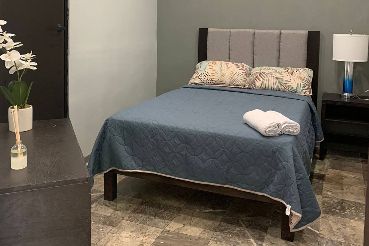 A neatly arranged bedroom with a bed, a nightstand, a lamp, a potted plant, and a painting on the wall.