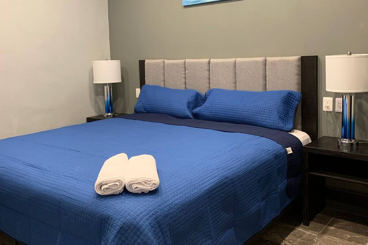 A hotel room with a large bed, two bedside tables with lamps, a painting of a moon on the wall, and a checkered floor.