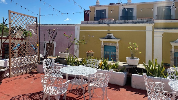 An outdoor patio with white metal chairs and tables, string lights, and potted plants. - Residencial Edzna (Campeche)
