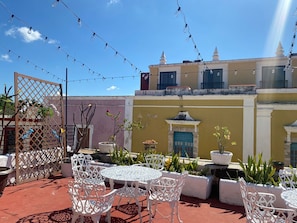 Un patio al aire libre con sillas y mesas de metal blanco, luces colgantes y plantas en macetas.