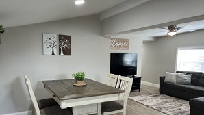 A dining area with a wooden table and chairs, a small potted plant, and a flat-screen TV in the background. - Cozy House with Large Deck (Hudson)