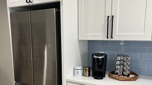 A kitchen with white cabinets, a stainless steel refrigerator, a coffee maker, and a decorative tray. - Cozy House with Large Deck (Hudson)