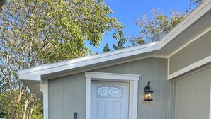 A building with a white door, a small porch, and a potted plant. - Cozy House with Large Deck (Hudson)