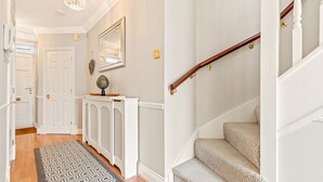 A hallway with a patterned rug, a white console table, and a staircase with a wooden handrail.
