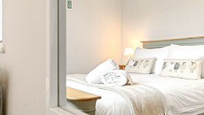 A neatly made bed with white linens and a white throw blanket, a bedside lamp, and a nightstand with a lamp.