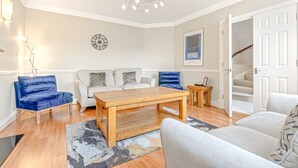 A living room with a wooden coffee table, two sofas, a blue chair, and a staircase leading to an upper floor.