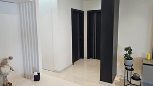 Ein modernes Interieur mit einem Flur, der zu zwei schwarzen Türen führt, einem kleinen Tisch mit einer Pflanze und einer dekorativen Gartenzwerg-Figur.