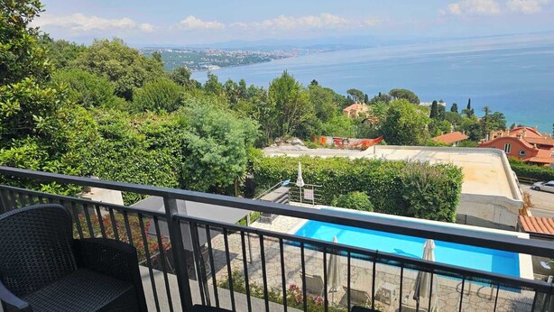 Ein Balkon mit Korbmöbeln, der auf einen Pool und die Küste blickt.