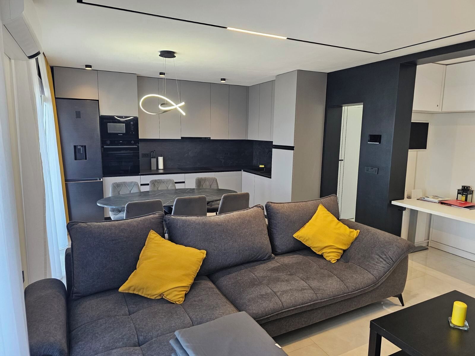 A modern living room with a grey sofa, two yellow cushions, a black coffee table, and a dining area with a black table and chairs.