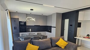 Ein modernes Wohnzimmer mit einem grauen Sofa, zwei gelben Kissen, einem schwarzen Couchtisch und einem Essbereich mit schwarzem Tisch und Stühlen.
