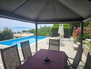 A covered outdoor area with a pool, seating, and a view of the sea. - GROZIC APARTMENTS **** OPATIJA - APARTMENT A1 (Opatija)