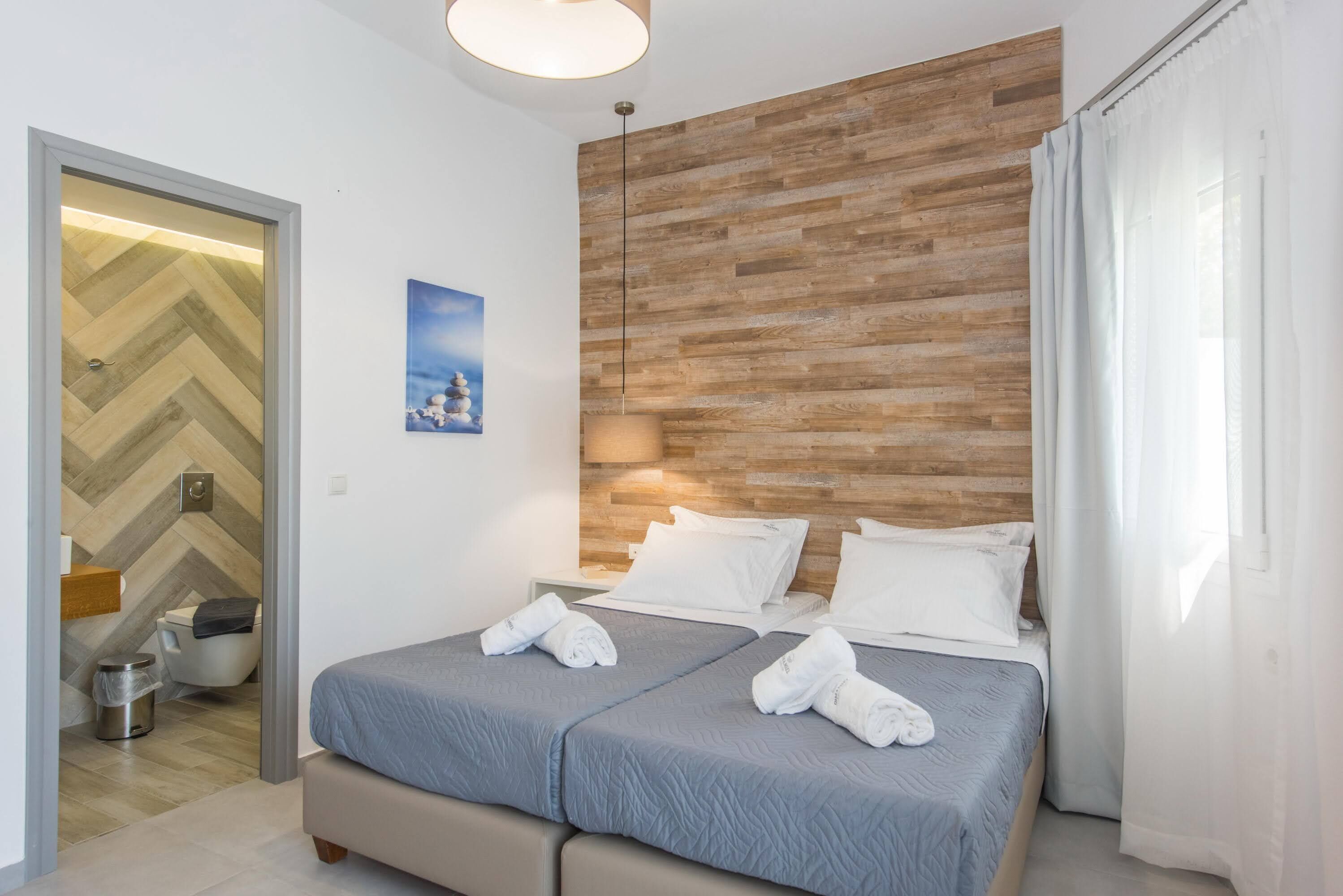 A hotel room with two beds, a wooden accent wall, a painting, and a bathroom with a herringbone floor pattern.