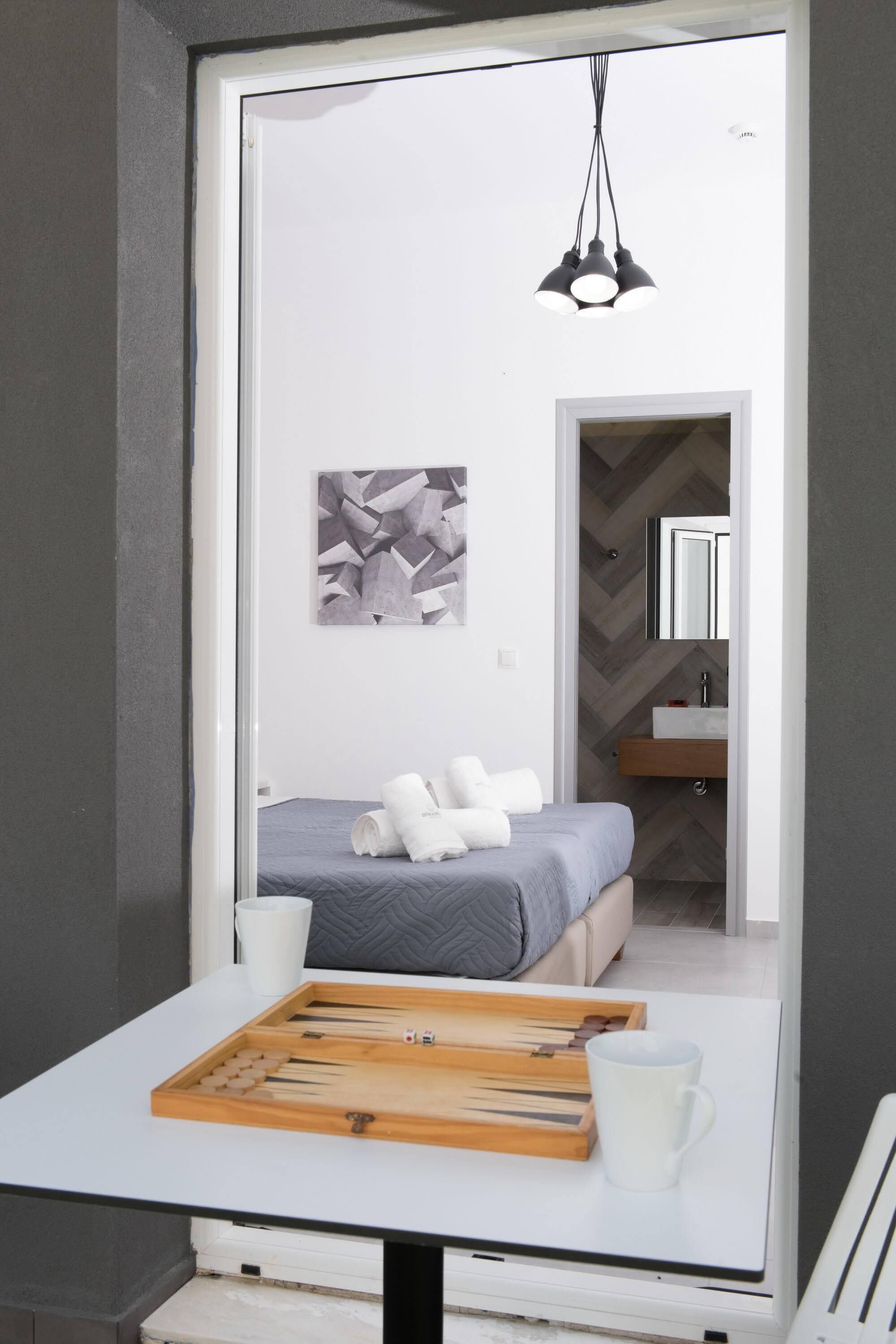 A modern bedroom with a bed, a bedside table with a board game, a cup, and a hanging light fixture.