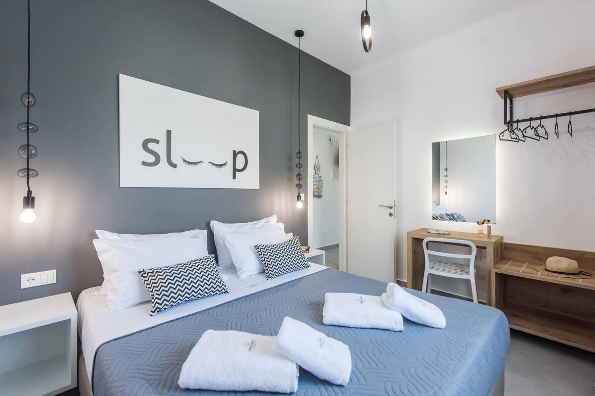 A modern hotel room with a bed, white nightstands, a desk, and a mirror.