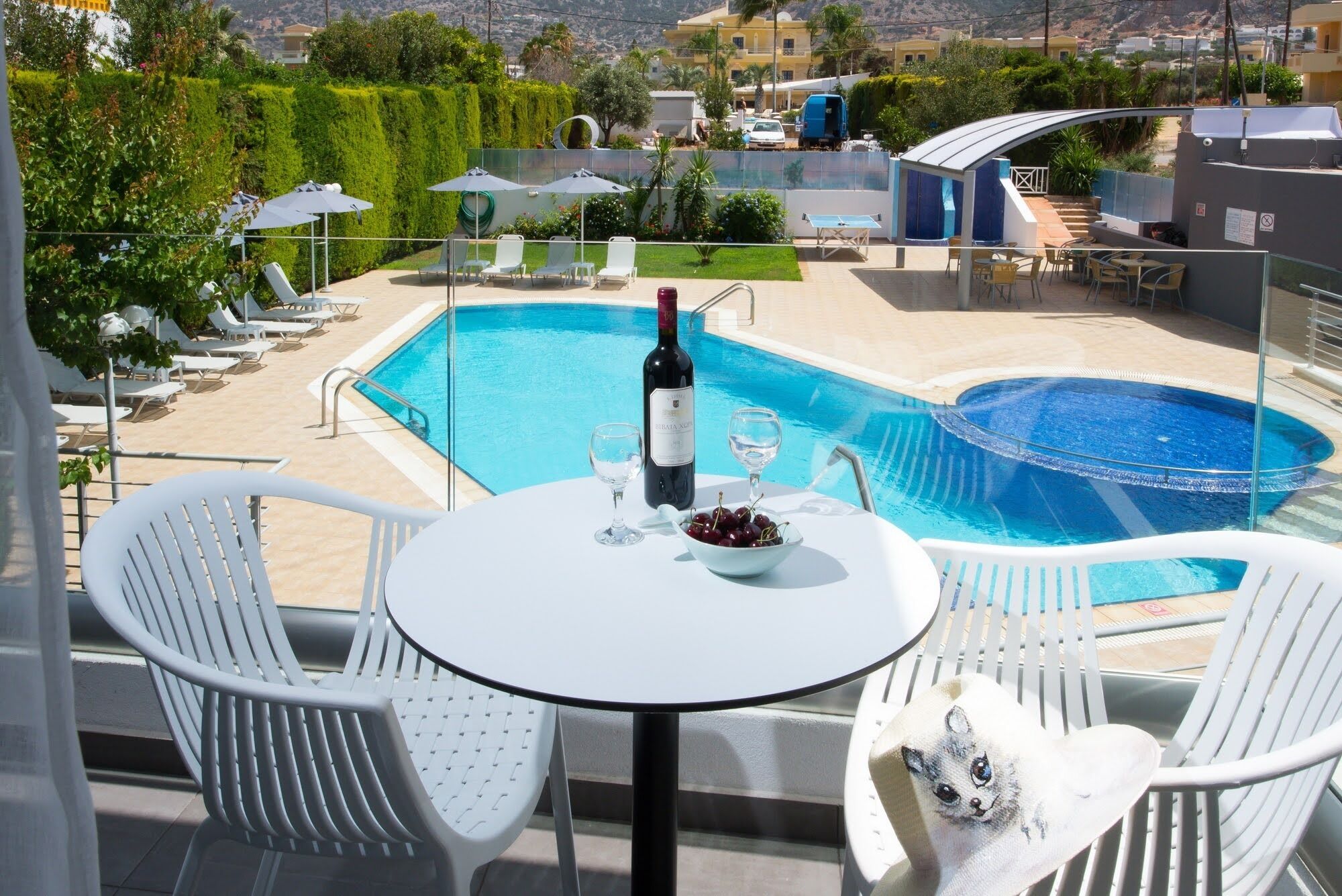 A poolside area with a table, chairs, and a bottle of wine.