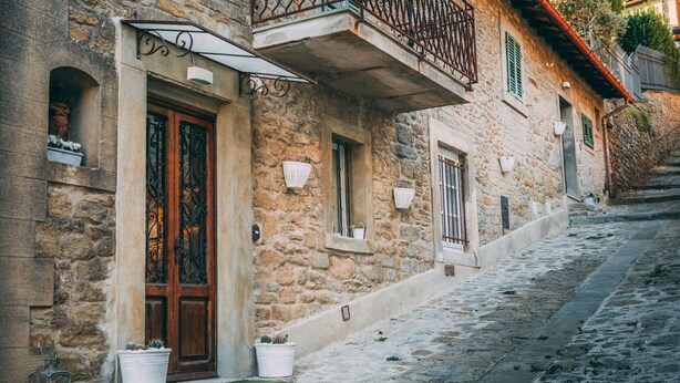 Un edificio de piedra con puerta de madera, plantas en macetas y una calle empedrada.