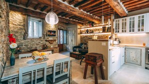 Una cocina rústica con paredes de piedra, vigas de madera y un comedor con mesa y sillas.