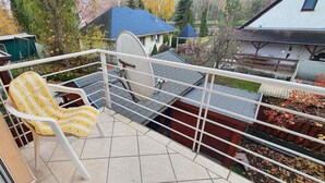 A balcony with a white chair, a metal railing, and a view of houses and trees. - Holiday apartment near the beach with internet (Siófok)