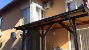 Ein überdachter Patio-Bereich mit einer Holz-Pergola, Klimaanlagen und einem Tisch mit Gartenmöbeln.
