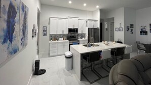 Una cocina moderna con armarios blancos, una isla central y un comedor con sillas.