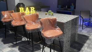 Una zona de bar con mostrador de granito, taburetes y un letrero de neón.