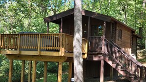 A wooden cabin with a balcony and stairs, surrounded by trees.