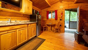 A wooden cabin interior with a kitchen, dining area, and a view through a door.