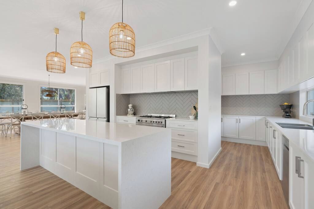 A modern kitchen with white cabinetry, a large island, and a herringbone-patterned backsplash.