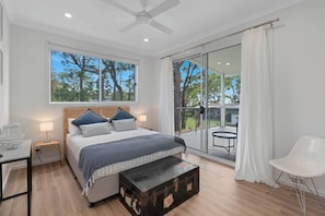 A bedroom with a bed, bedside table, lamp, suitcase, and a view of the outdoors through a sliding glass door.