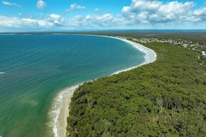 An aerial view of a coastal area with a beach and dense forest.