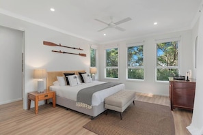A bedroom with a bed, bedside tables, a ceiling fan, and large windows.