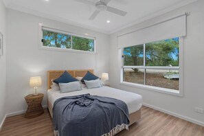 Ein Schlafzimmer mit einem Bett, zwei Fenstern, einem Deckenventilator und einem Korbtisch.