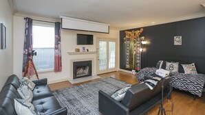 A living room with a fireplace, a sofa, a bed, and a projector. - Movie Nights Nash! 2bd Townhome off WEST END! 8 min-> DT! (Nashville)
