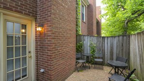 A brick building with a door and windows, a wooden fence, and outdoor seating with chairs and a table. - Movie Nights Nash! 2bd Townhome off WEST END! 8 min-> DT! (Nashville)